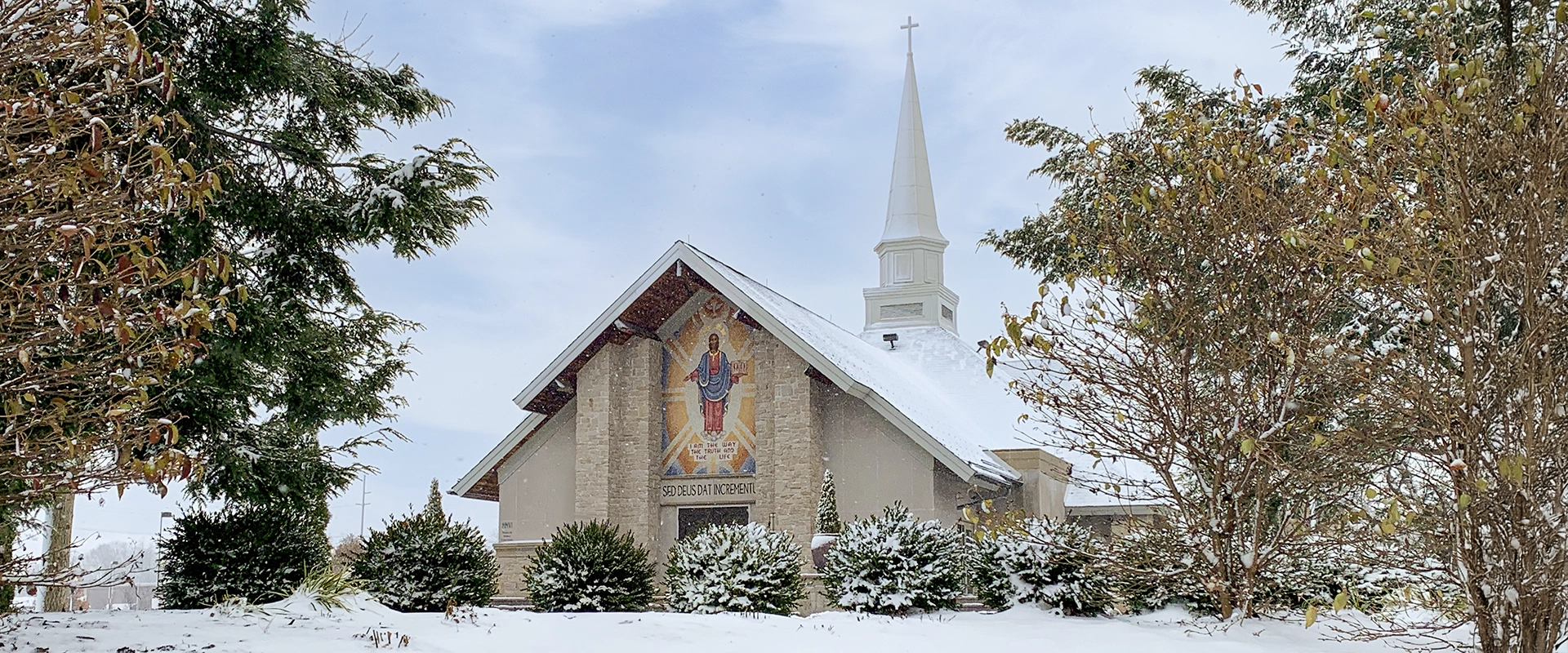 Our Lady of Perpetual Help Chapel at Walsh University on a winter morning, with snow covering the lawn and rooftops, trees framing the building, and a soft sunrise sky overhead.