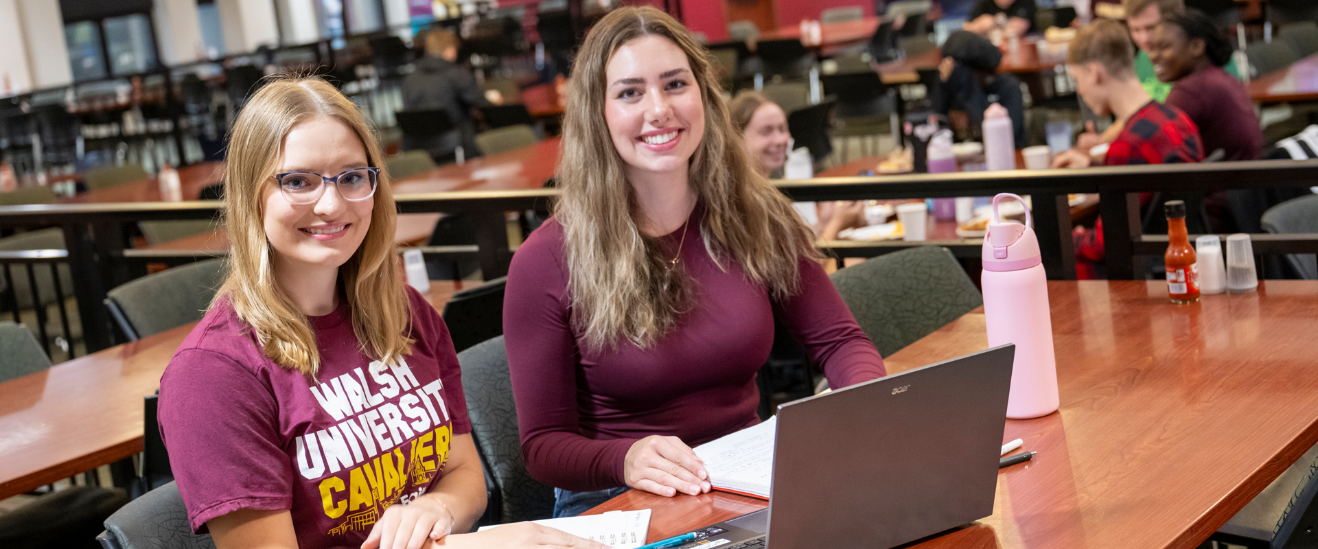 Two female students sitting at a table and smiling at the camera.