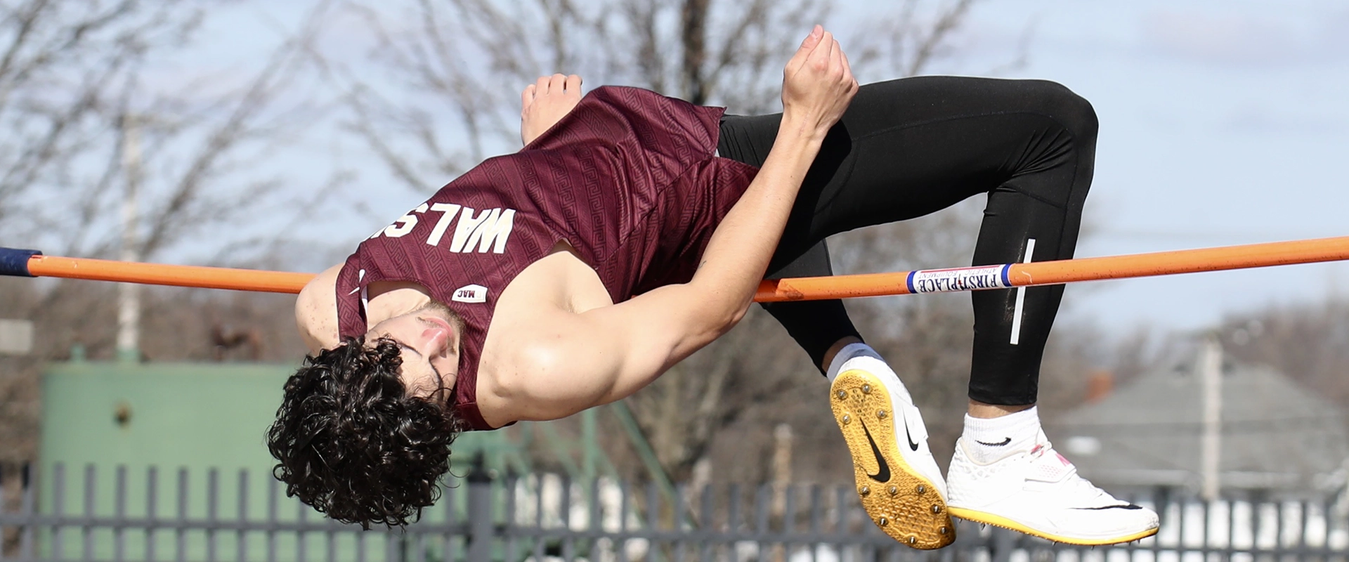 A Walsh University high jumper wearing a maroon uniform clears the bar during a Track meet