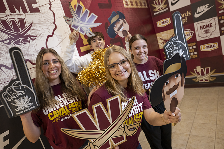 A group of students in maroon and gold attire, holding various school spirit props.