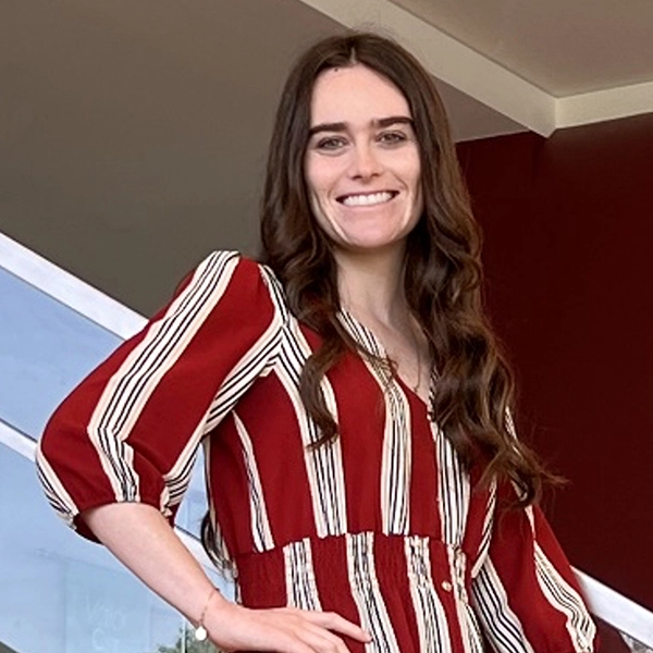 Smiling woman in a striped red and white blouse posing confidently against a modern architectural backdrop.