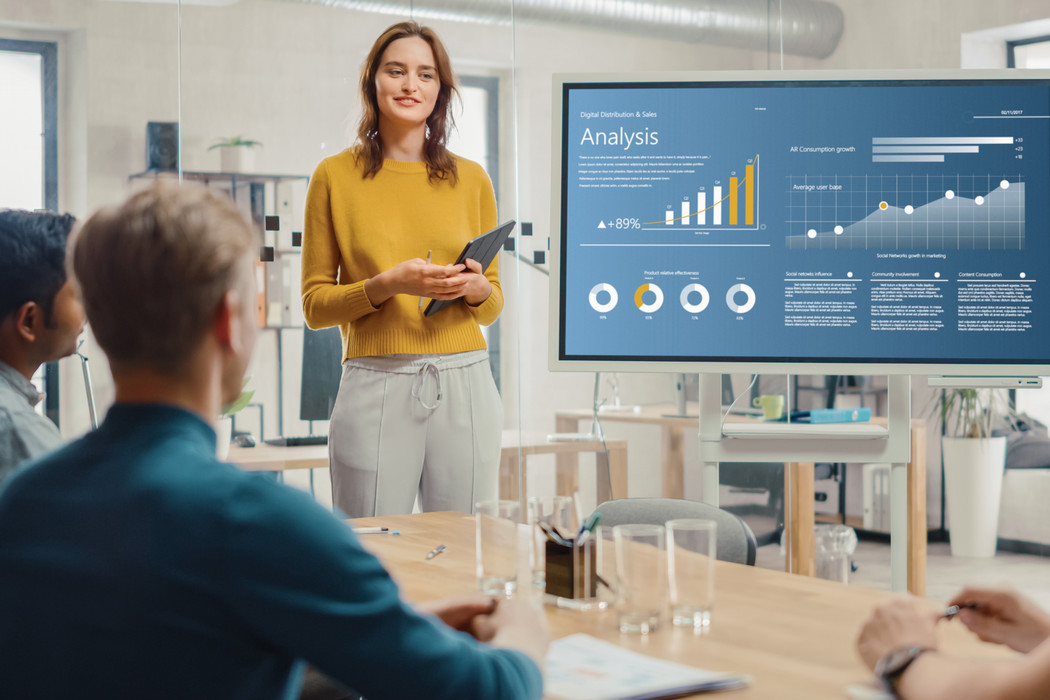 young professionals attending a meeting where analytic data is displayed on a tv screen