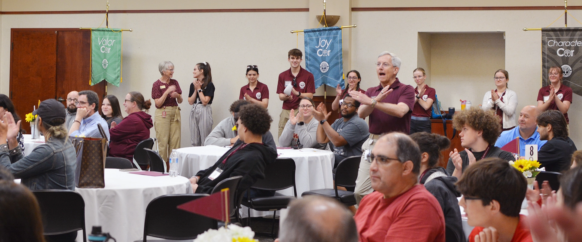 President Tim Collins addresses a group of students and parents with the Swords Up! hand gesture during a summer orientation session