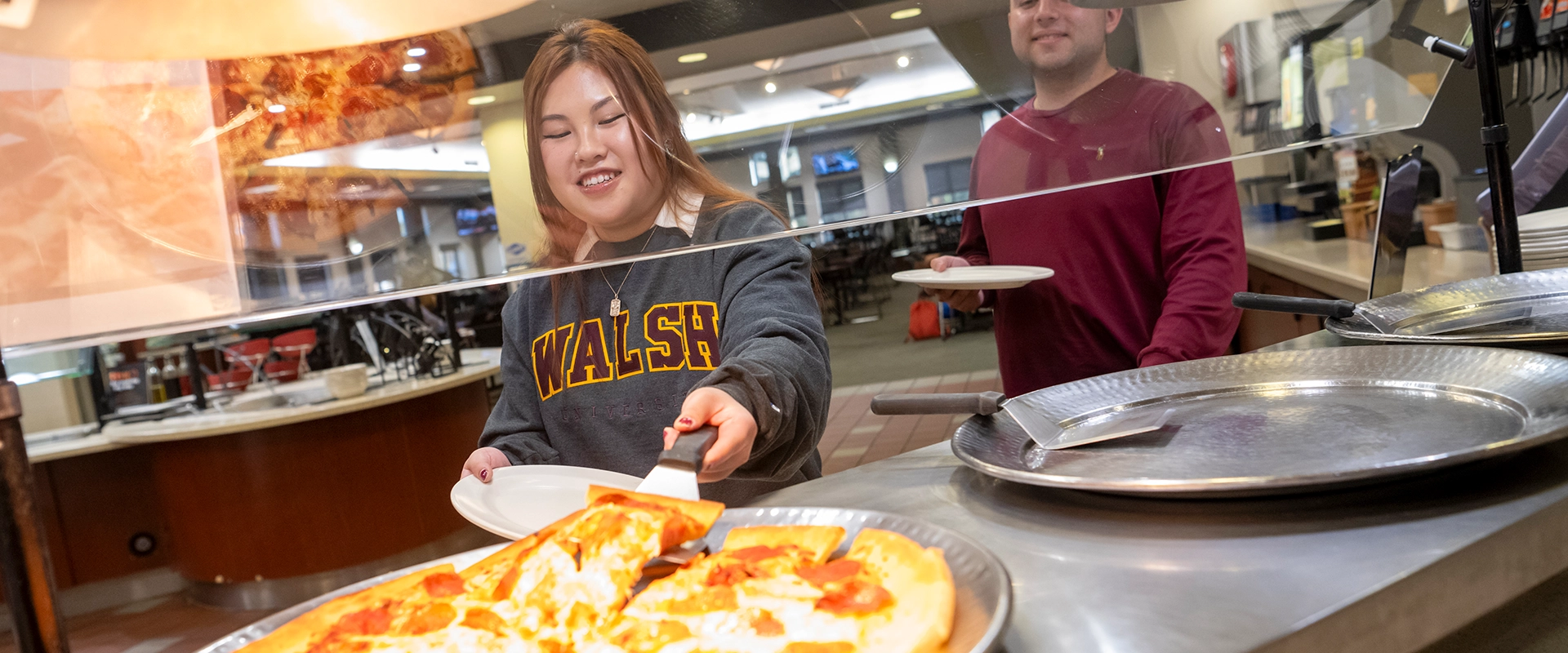Photo of a student grabbing a slice of pizza at the dining hall