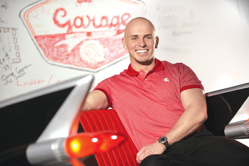Business student in a red polo, seated in a modern working space with a white board behind them.